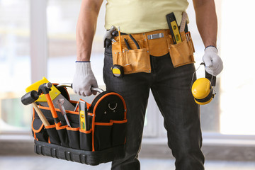 Male builder holding bag with tools and headphones in office