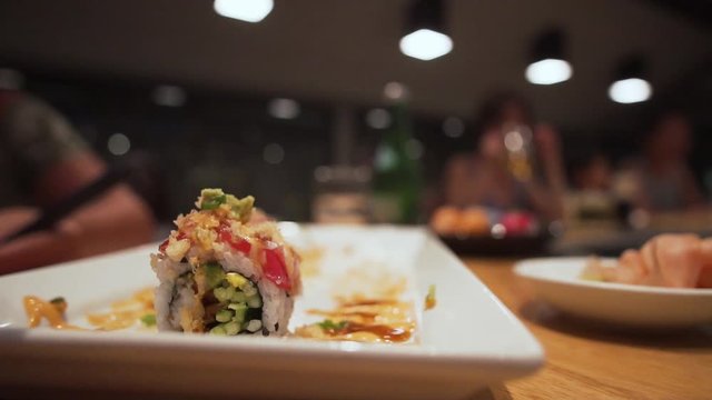 static shot of subject eating sushi from plate with chopsticks