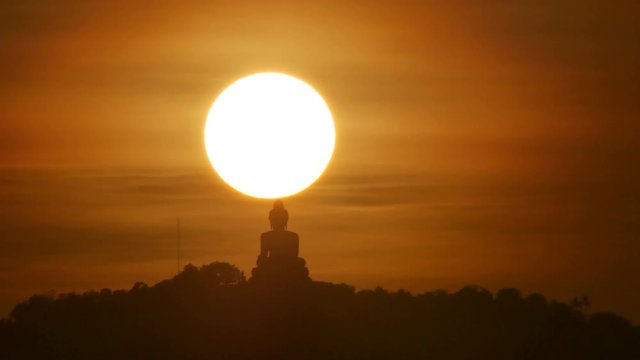 hue sunset over and behind silhouette Phuket big buddha statue on hilltop with many big trees high mountain in the beautiful evening colourful  orange twilight sky , attraction tourist photo spot
