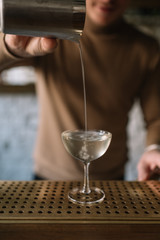 Bartender pouring a cocktail from a mixing pitcher into a cooled glass. Smooth image with shallow depth of field.
