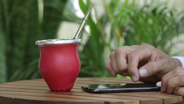Close-up of man's hands using smartphone relaxing and drinking yerba mate tea in cafe sitting at table alone. People, modern technology and drinks concept. Slow motion.