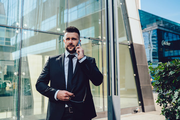 Frowning businessman having smartphone conversation on street