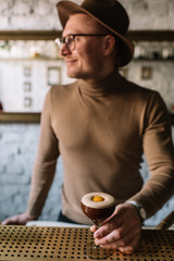 Bartender holding on his hand glass with espresso martini cocktail decorated with slice of orange zest. Smooth image with shallow depth of field.