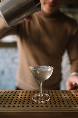 Bartender pouring a cocktail from a mixing pitcher into a cooled glass. Smooth image with shallow depth of field.