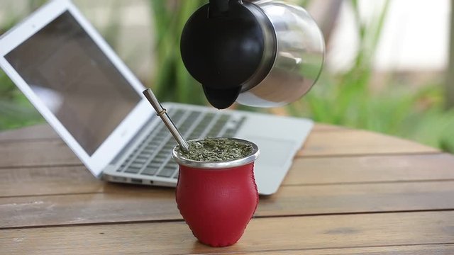 Woman working on laptop and drinking yerba mate tea in home office. Female hands typing on laptop, drinking hot yerba mate tea. Slow Motion.