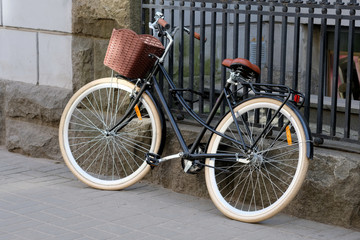 A leisure bike with a brown basket is parked near a metal fence. City bike for walking and shopping trip. Bicycle theft unreliable locks.