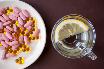 Tablets and fish oil in a plate and a transparent Cup with lemon on a brown background