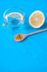 Wooden spoon with fish oil, cut lemon and a Cup with water and a slice of lemon on a blue background, place for text