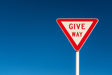 A give way sign against a clear bright blue sky, copyspace to the left.