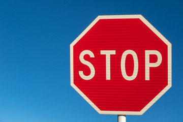 A bright red stop sign against a perfect blue sky, copy space to the left.