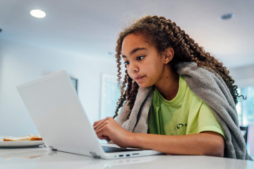 Girl wrapped in blanket studying on laptop computer