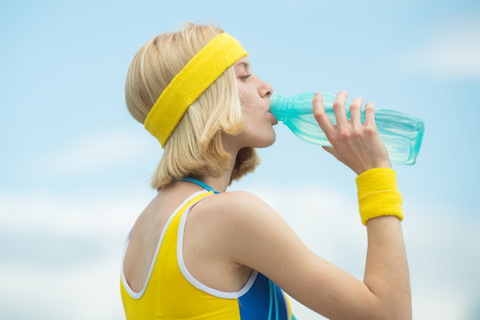 Fitness woman. Midsection of sporty woman with measure tape around waist holding water bottle in park over sky backgroung.