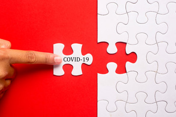 Hand holding piece of white puzzle on blue background with word COVID-19. Coronavirus pandemic prevention social distance and self-quarantine.