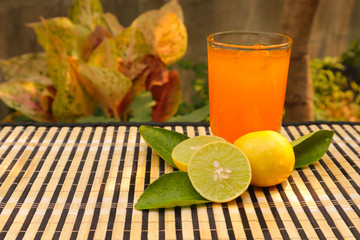 Fototapeta premium Fresh lemon slice with green leaves and lemon juice in clear glass put on bamboo table and blur background of tree