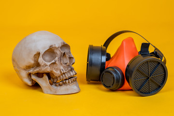 Human skull next to a respirator. Skull and a respirator on an orange background. Concept -...
