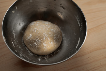 Overhead view of a ball of pizza dough with flour in an iron bowl on a wooden table