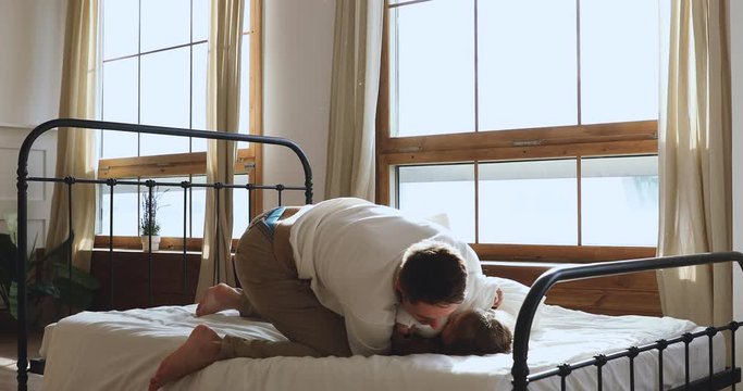 Full length happy young father fighting pillows with little preschool child daughter in bedroom. Energetic small cute kid girl playing having fun, enjoying morning leisure time with active dad on bed.