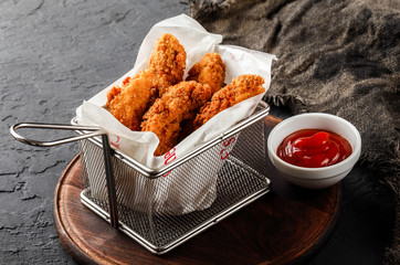 Fried crispy chicken nuggets with ketchup on black stone background. Hot fast food, close up