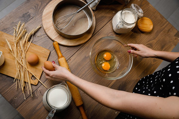 The confectioner prepares the dough, bread, cakes. Preparation and work with flour, eggs, milk and ingredients. Delicious food, recipes, cooking, gastronomy, on a dark background and wooden table.