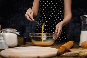 The confectioner prepares the dough, bread, cakes. Preparation and work with flour, eggs, milk and ingredients. Delicious food, recipes, cooking, gastronomy, on a dark background and wooden table.