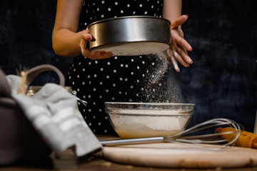 The confectioner prepares the dough, bread, cakes. Preparation and work with flour, eggs, milk and ingredients. Delicious food, recipes, cooking, gastronomy, on a dark background and wooden table.