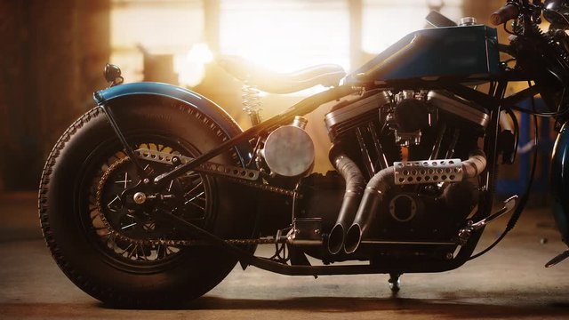Custom Bobber Motorbike Standing in an Authentic Creative Workshop. Vintage Style Motorcycle Under Warm Lamp Light in a Garage. Profile View.