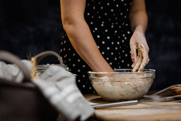 The confectioner prepares the dough, bread, cakes. Preparation and work with flour, eggs, milk and ingredients. Delicious food, recipes, cooking, gastronomy, on a dark background and wooden table.