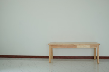 Modern long wooden chair is located in the empty room on the white wall.