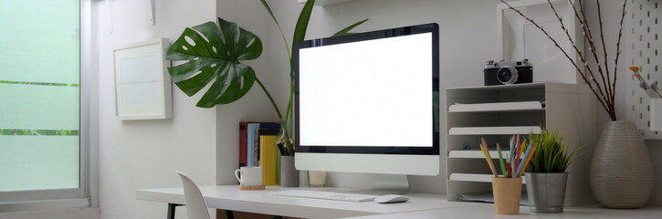 Cropped shot of minimal office room with blank screen computer, office supplies and decorations