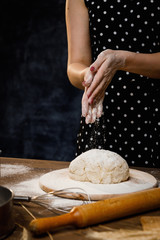 The confectioner prepares the dough, bread, cakes. Preparation and work with flour, eggs, milk and ingredients. Delicious food, recipes, cooking, gastronomy, on a dark background and wooden table.
