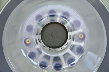  Closed laboratory centrifuge with test tubes in compartments. View from above. In the process of rotation.