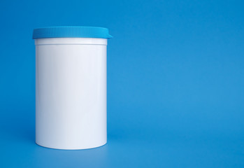 Pill dispenser can or jar. Single white large plastic container with blue screw top, reusable. Used to dispense and store supplements, medicine, tablets. Soft blue background. Copy space.