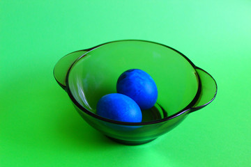 Two blue eggs in a transparent black plate. Green background.