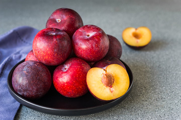 Red organic plums against grey stone background
