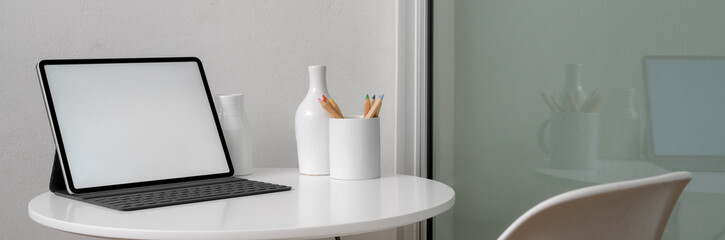 Cropped shot of portable workspace with mock-up tablet and ceramic decorations on white circle table