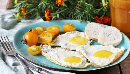 Fototapeta na wymiar sunny breakfast life style, fried eggs and yellow cherry tomatoes. on a blue plate. yellow and blue