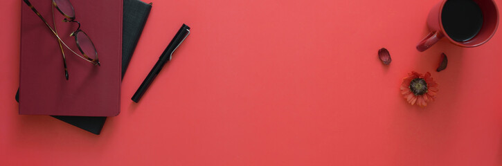Top view of workspace with diary notebooks, eyeglasses, coffee cup and copy space on pink table