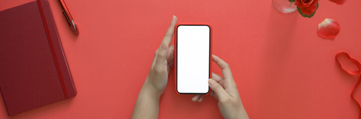 Top view of a woman holding blank screen smartphone while sitting at creative workspace