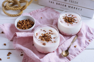 Bowl of granola with natural yogurt and raspberries. On a white wooden background and a pink fabric napkin. Copper spoon.