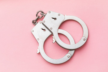 Closed handcuffs on a pink background, top view