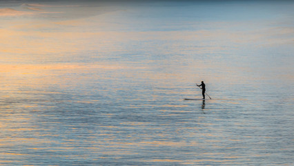 Person paddling on the water surface during sunset, silhouette shot from New Brighton Beach,...