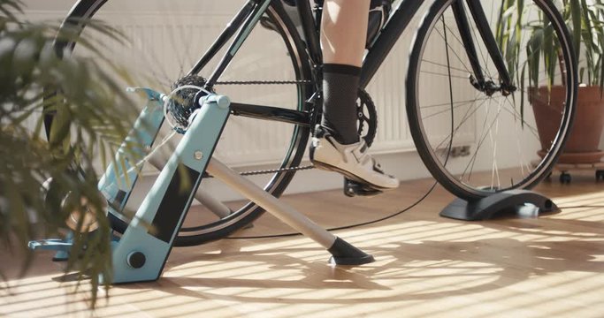 Woman riding indoor sports bicycle trainer staying home for wellbeing and self care fighting anxiety maintaining health and immunity during isolation crankset detail
