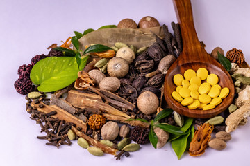 Ayurvedic medicine concept. Ayurvedic drugs in wooden spoon, assorted spices and green leaves on white background