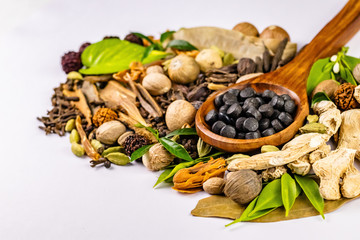 close-up view of assorted Indian Spices with green leaves and ayurvedic drugs in a wooden spoon on white background. Herbal concept