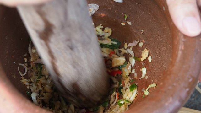 Fresh chilli and garlic pounding in mortar on wooden table, Hand pounding chilli and garlic in stone mortar. Selective focus.