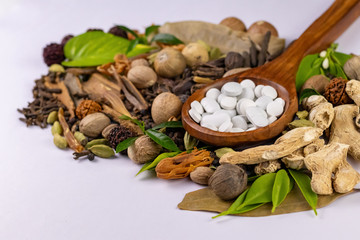 High angle shot of white tablets in closeup with dried herbs and white surface in the background. Herbal and Unani concept