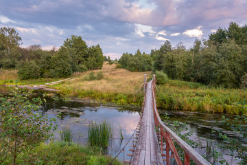 Suspension bridge over the forest stream at sunset