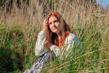 Beautiful happy woman sitting in grass in white sweater