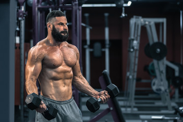 Fototapeta na wymiar Muscular athletic bodybuilder working hard in gym on dark background