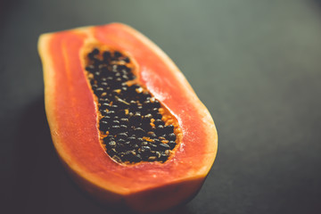 Papaya halves on a black background. Cut papaya with orange flesh and bones. Exotic sweet fruit.